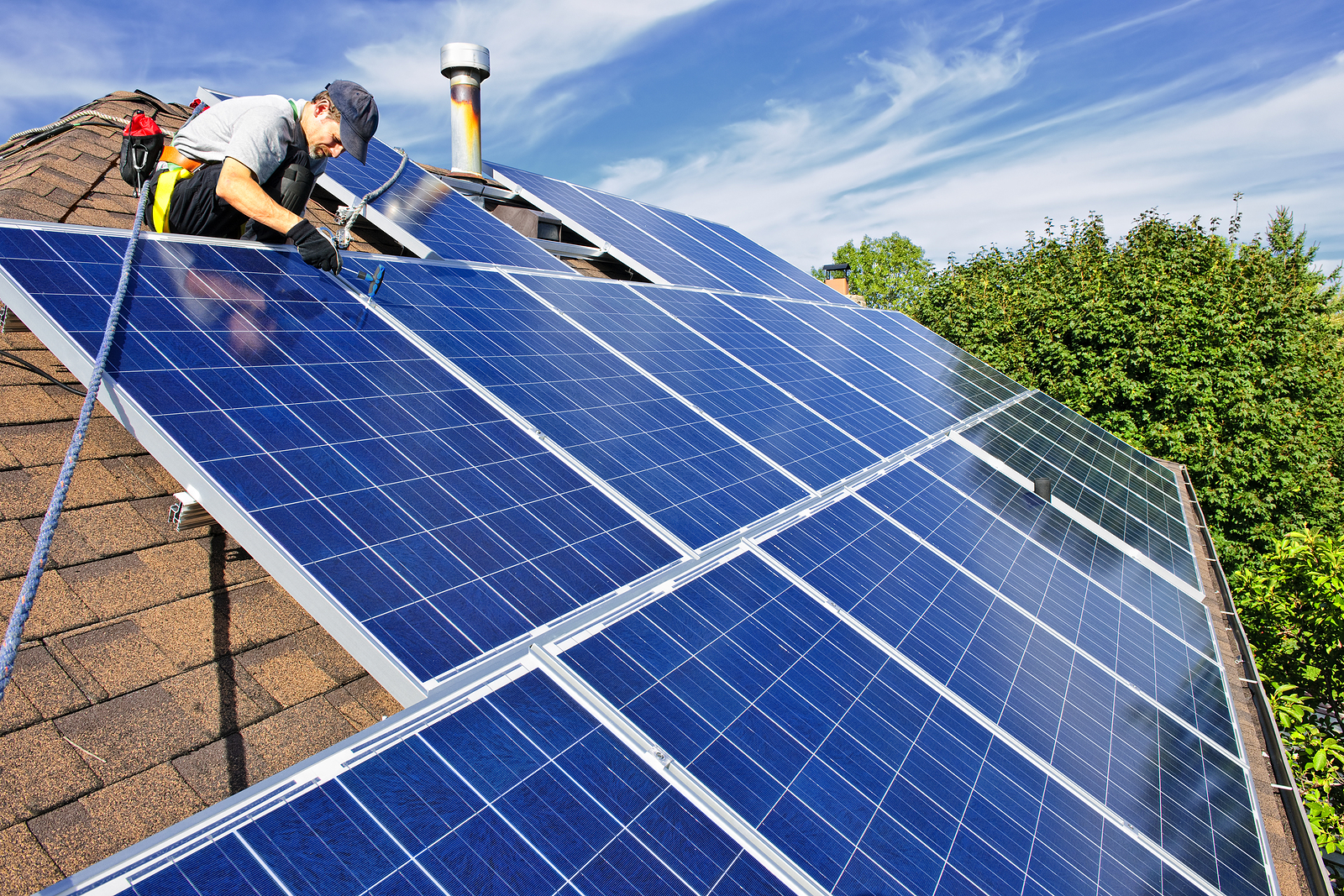 Man installing solar panels on a roof. Learn how you can lower your average monthly electric bill with solar panels in this article.