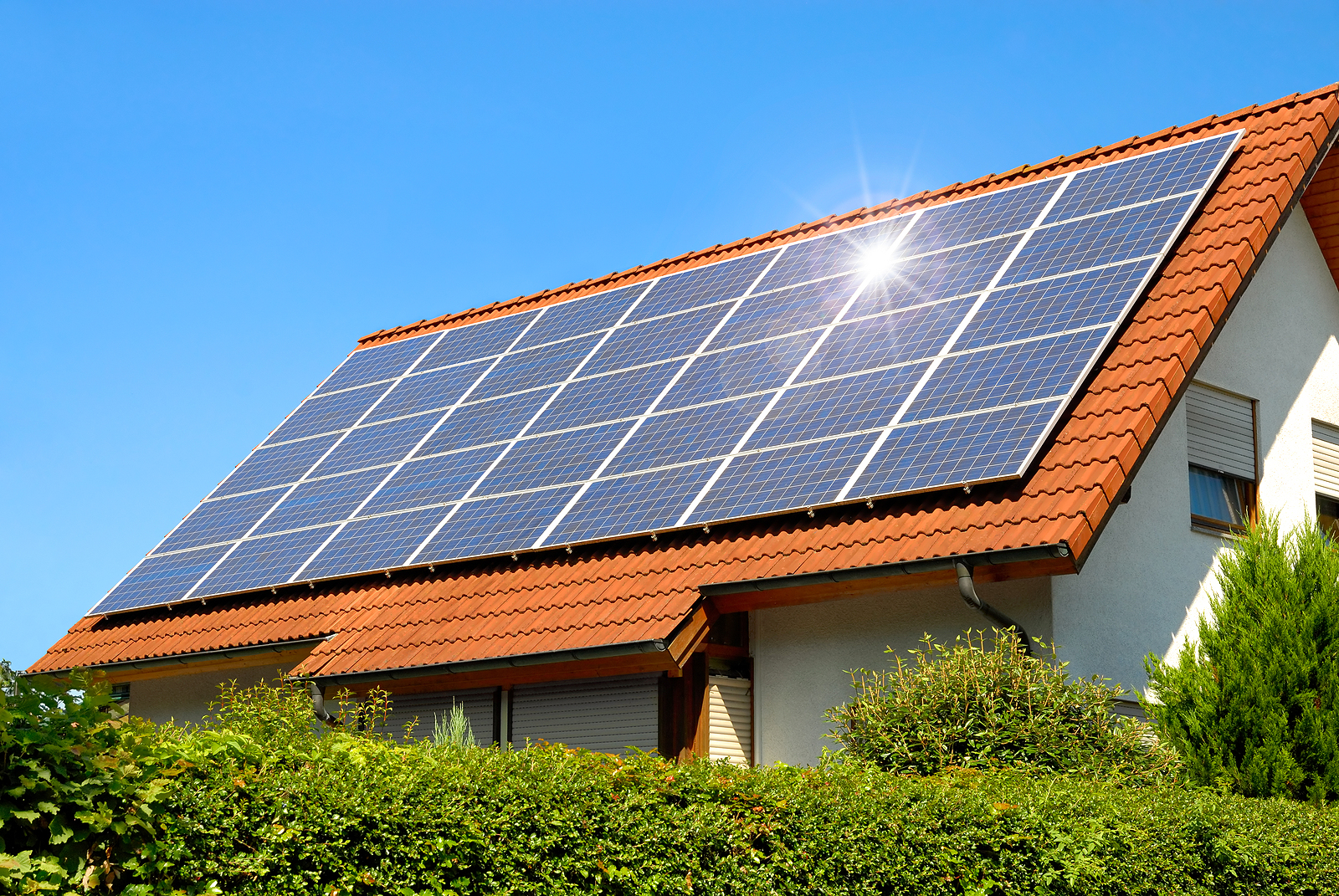 Solar panel on a red roof reflecting the sun and the cloudless blue sky - learn more about when do solar panels break.