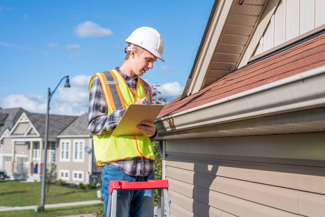 Roof inspector standing on a ladder and providing a roof inspection to a house.