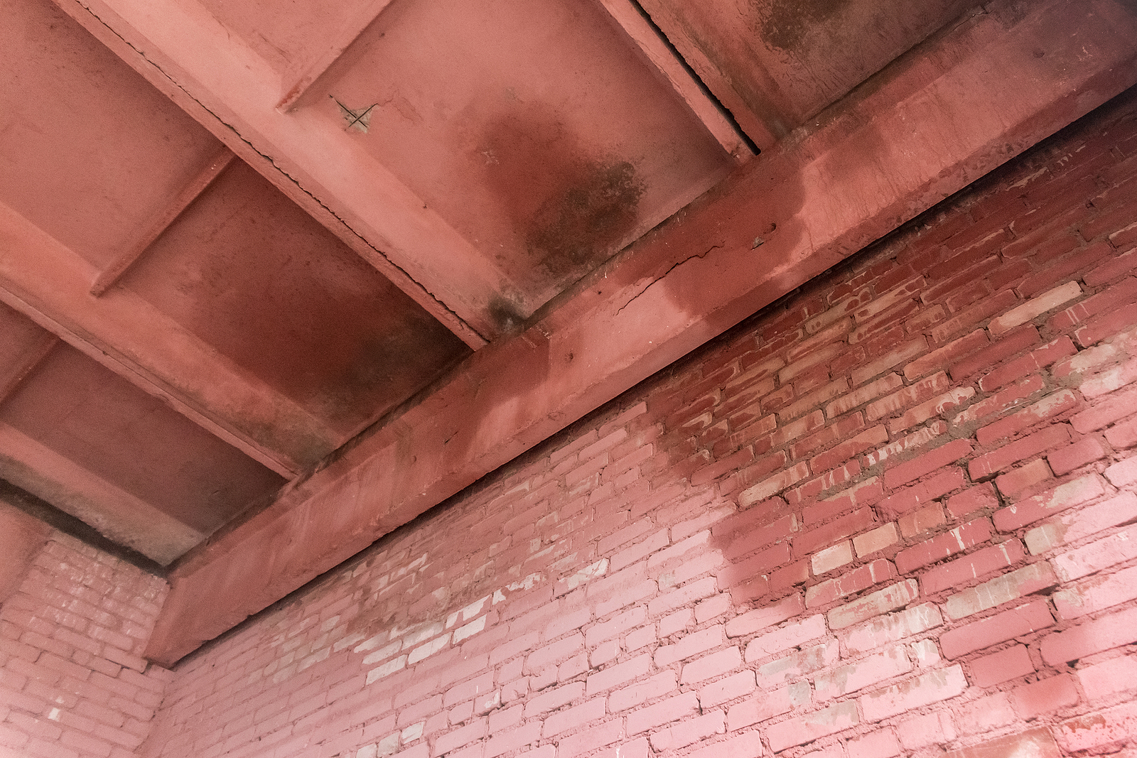 Old brick facade wall with leaking roof and wet water stain on the surface. Learn more about the signs of roof leak.